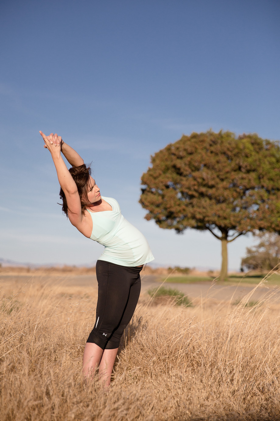 Pregnant expectant mother doing yoga in grassy field with tree