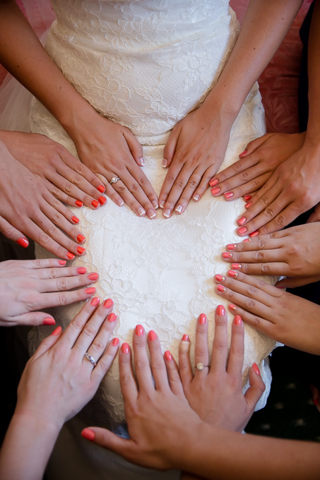 Bride sitting and bridesmaids hands on her lap