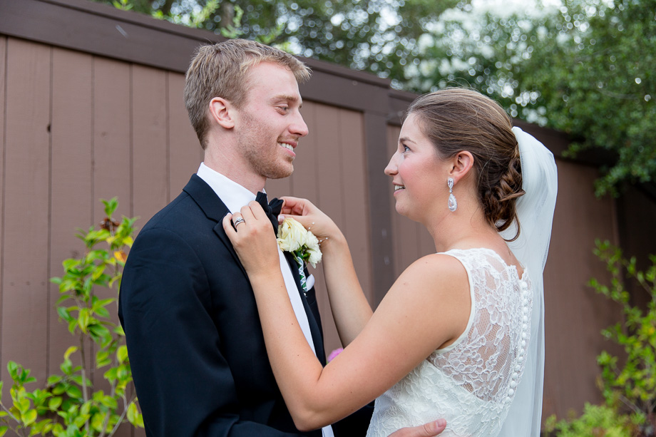 Bride helping groom fix and straighten his tie and boutinierre