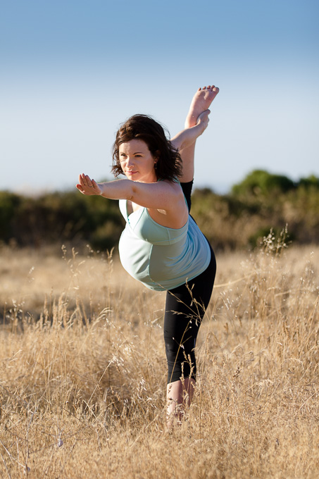 Maternity shoot of pregnant expectant mother holding yoga pose with sunlight on the side of her face