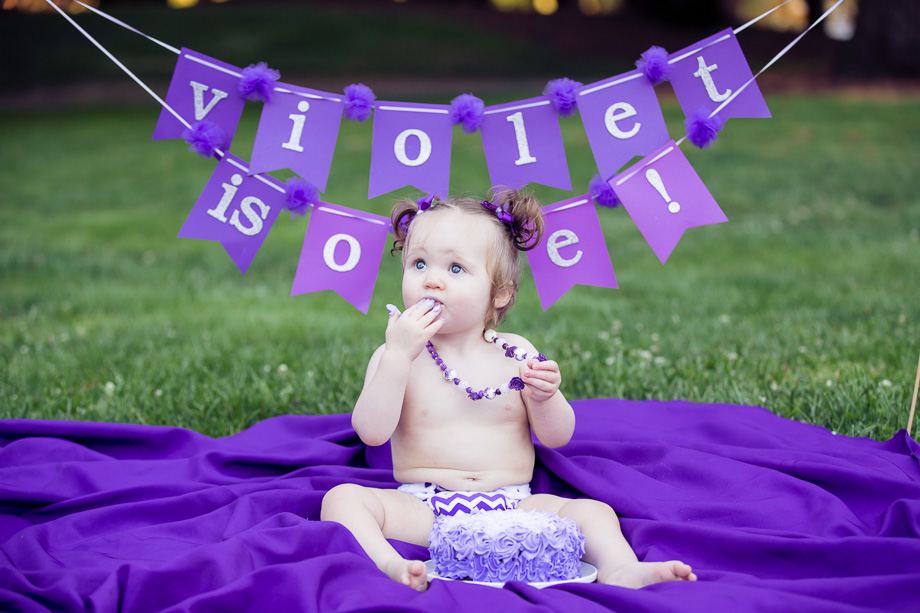 Baby Violet putting her hand in her mouth trying out her first bite of birthday cake