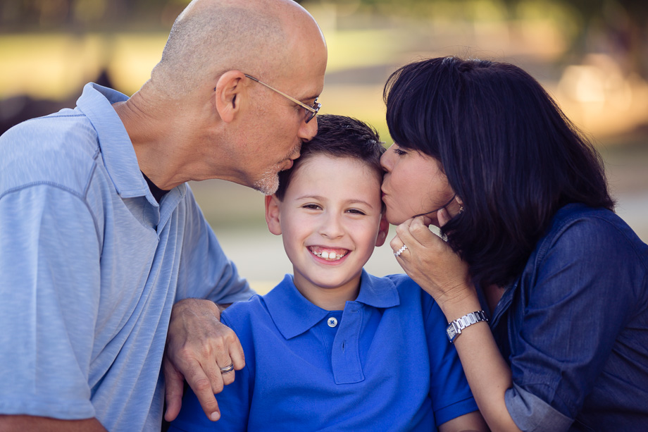 family photography session of parents kissing son on his forehead