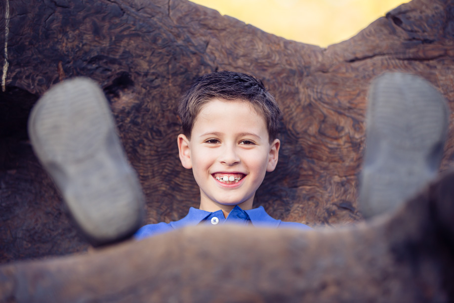happy boy sitting on a piece of wood with his face between his feet