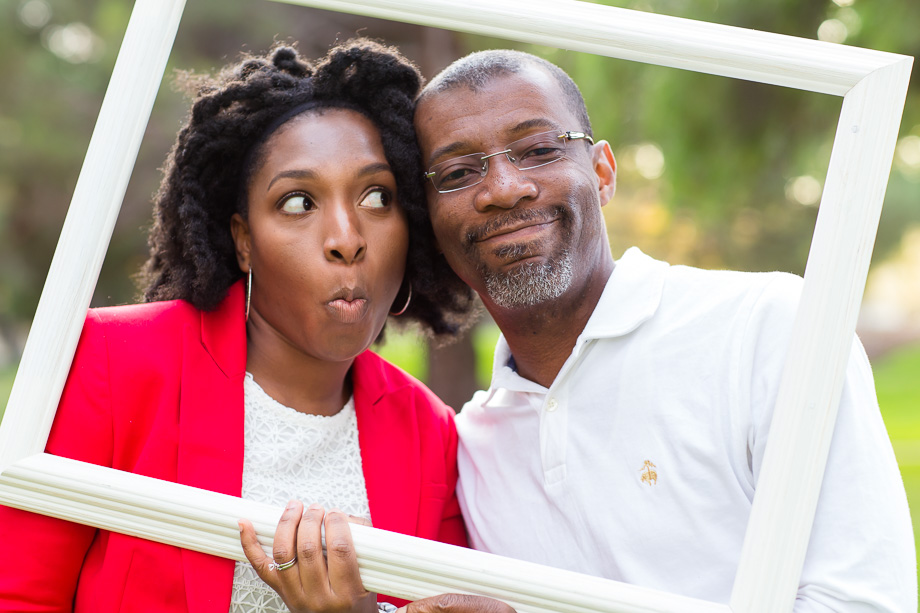 wife making silly face at smiling husband behind empty wooden picture frame