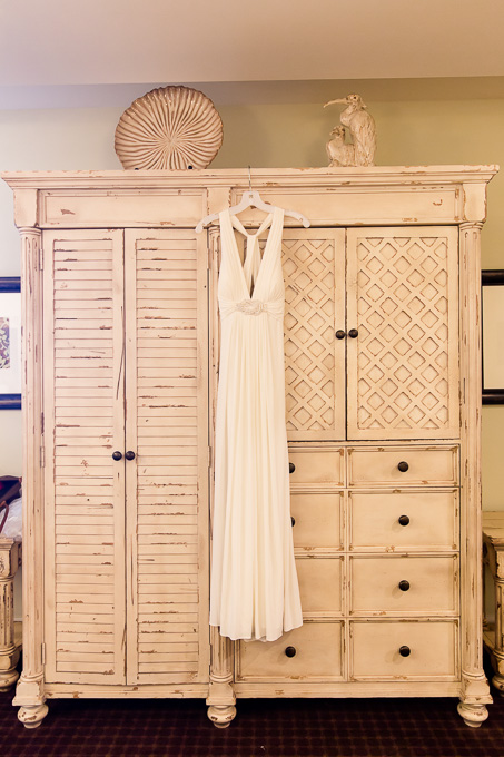 Sleek wedding gown hanging on a rustic white cabinet