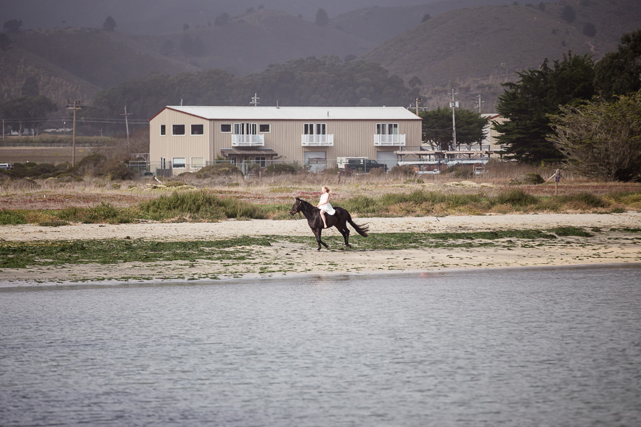 The bride riding a horse for her grand entrance for their beach ceremony in Half Moon Bay