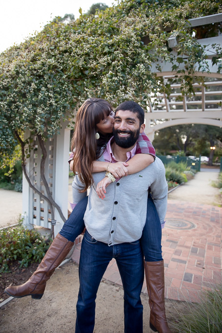wife piggyback riding on husband and kissing in front of an arch at Gamble Garden