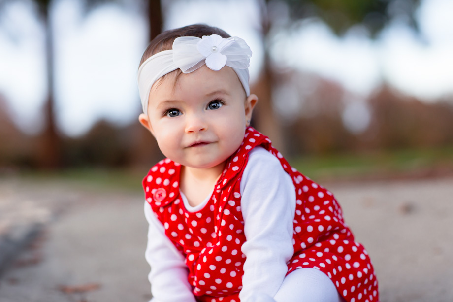 Adorable red polka dot dress and a white floral headband for the cute smiling nine-month-old baby for the family Christmas cards