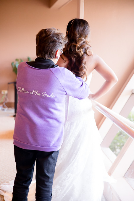mother of the bride in her uniform sweater helping the bride with the back of her dress