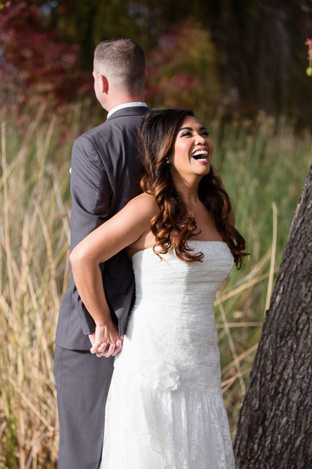 first touch instead of first look, bride laughing while holding hands behind her back with her groom