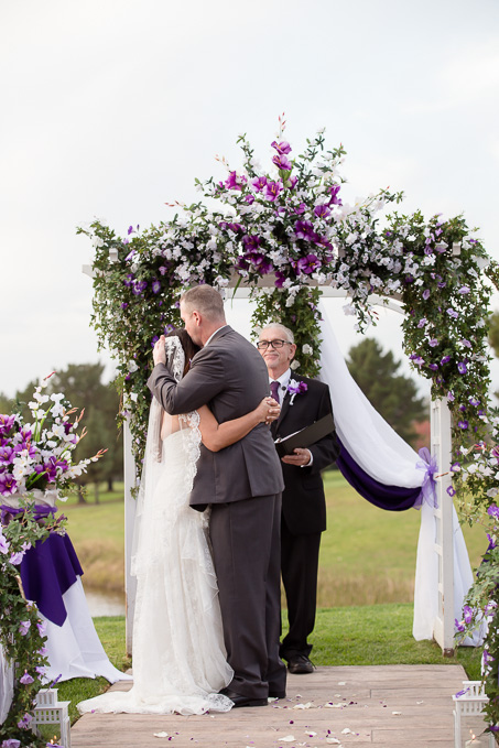 Happy couple kissing each other as husband and wife under a purple arch at the Boundary Oak Golf Club
