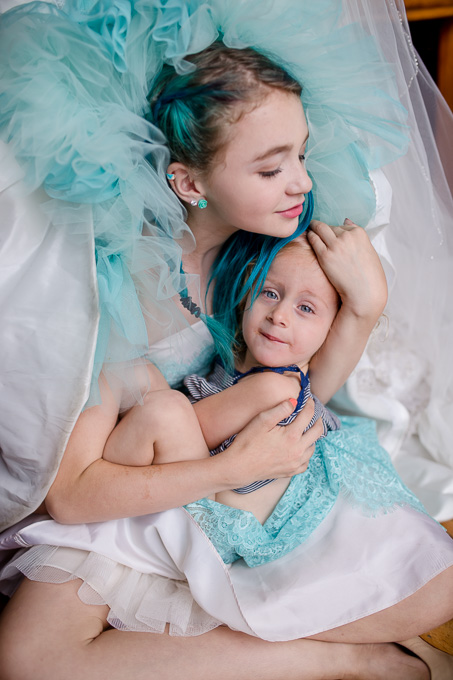 junior bridesmaid with flower girl sitting under brides blue wedding gown under skirt