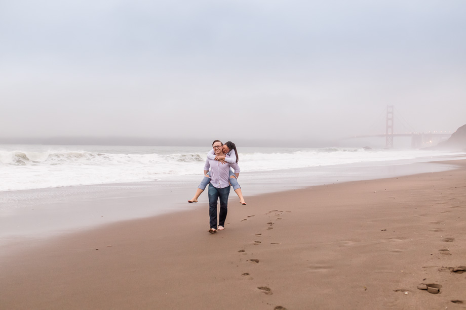 piggyback ride running along foggy Baker Beach in the wet sand