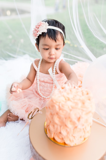 curious baby touching her one year birthday cake